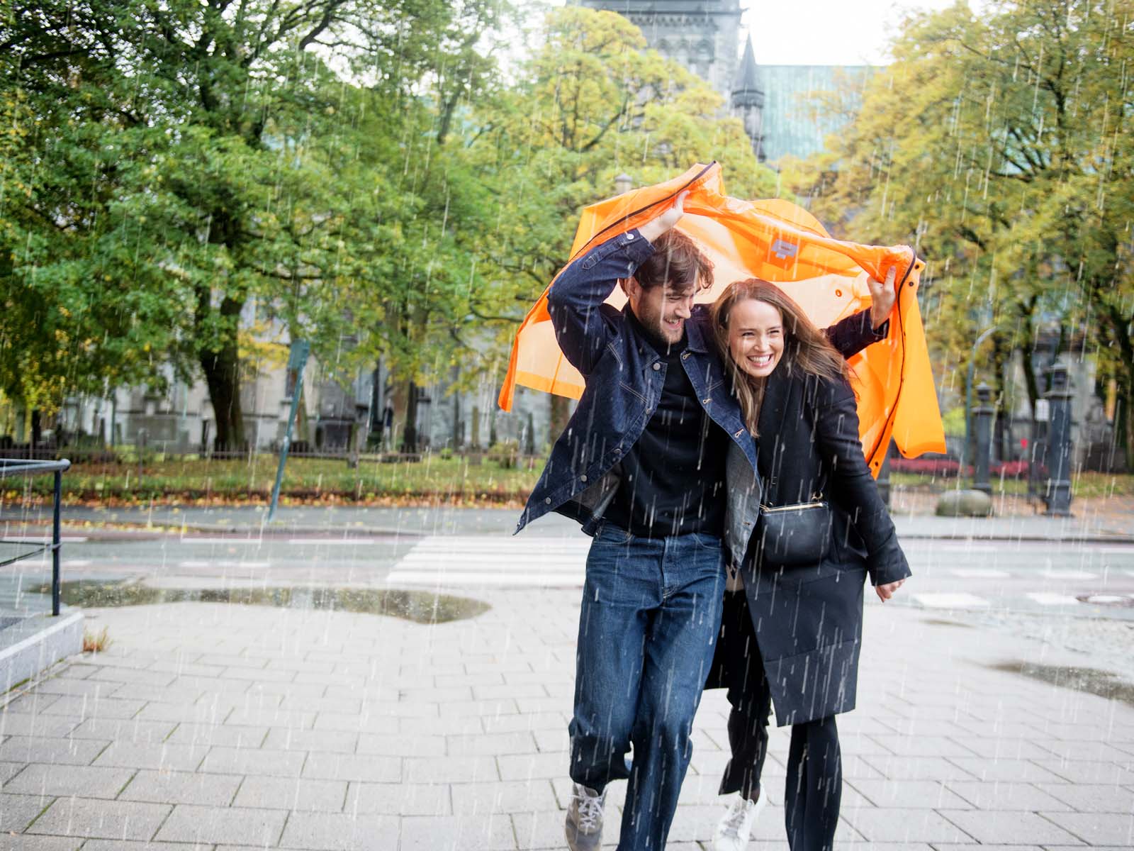 Ungt par i regnet Ungt par løper i regnet med en oransje jakke over seg