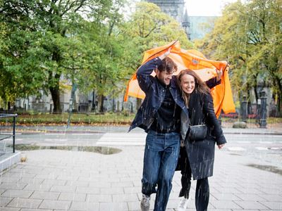 Ungt par i regnet Ungt par løper i regnet med en oransje jakke over seg